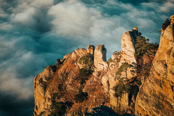 Majestic rocks with pine trees on the background of clouds in the sunset sky. - 616913194