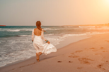 Model in boho style in a white long dress and silver jewelry on the beach. Her hair is braided, and there are many bracelets on her arms.