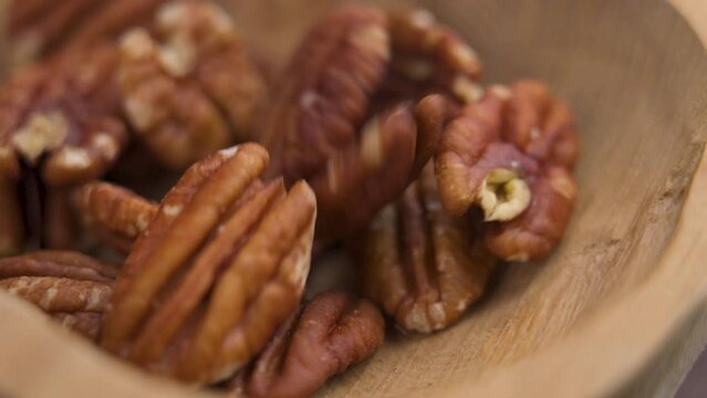 Tasty peeled pecan nuts falling into a rustic wooden brown bowl close up in slow motion