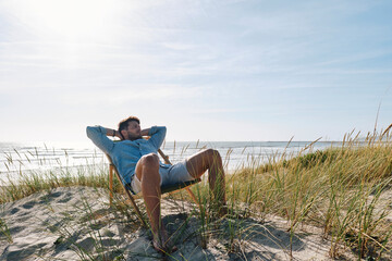 Man relaxing on chair at beach on sunny day