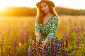 Close up on hand of happy young woman in style dress on blooming fragrant lavender fields with endless rows. Warm sunset light. Nature, vacation, relax and lifestyle. 