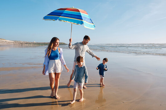 Father holding sunshade walking with family at beach on sunny day
