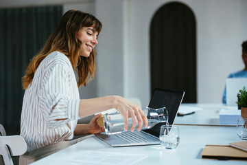 Happy businesswoman pouring water in glass at desk