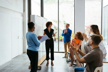 Happy young businesswoman with colleagues applauding in office