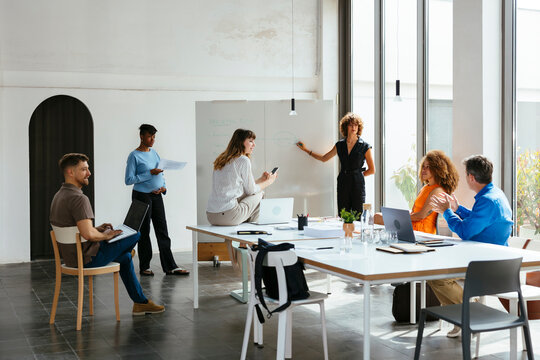 Businesswoman standing by whiteboard and having discussion with colleagues - Powered by Adobe