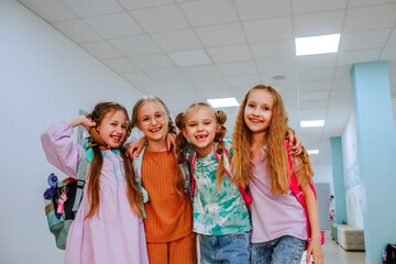 Happy schoolgirls standing with arm around in school corridor