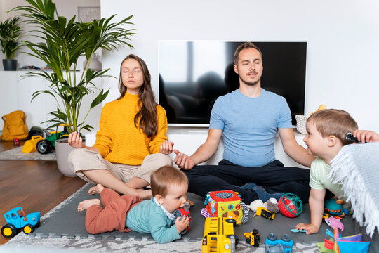 Parents meditating with children playing in living room at home