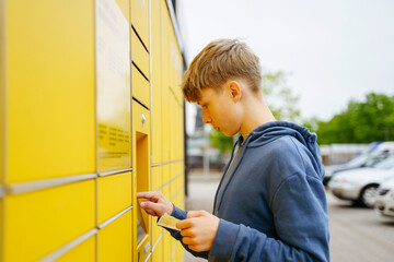 Blond boy with ticket entering data in parcel locker machine