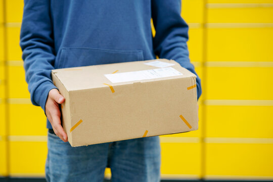 Boy holding package standing in front of yellow parcel locker