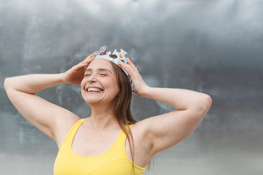 Happy woman wearing crown in front of wall