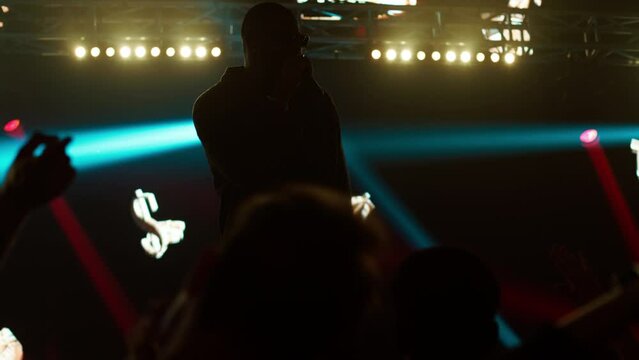 African-American Black rap artist performing his gig in front of a concert crowd on a stage of a large venue, surrounded by bright flashig lights