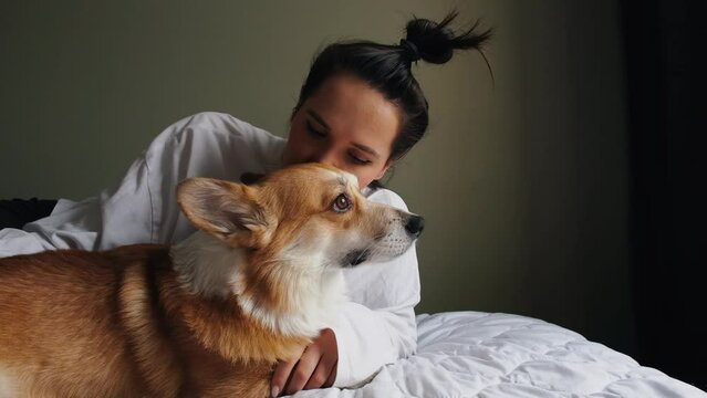 portrait of a girl hugging and kissing her cute curious corgi dog on a white bed