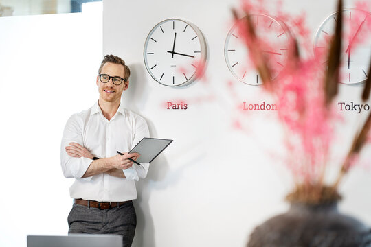 Happy businessman leaning with tablet PC on wall