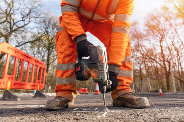 Close-up of a builder using a cordless hammer drill to drill holes in the road at the location...