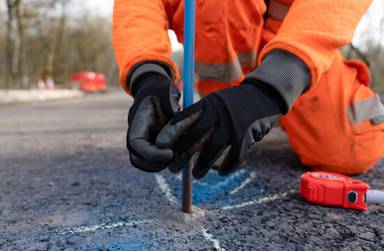 Builder marking future finish road levels on a road setting out steel pins with yellow electric tape on a road improvement project