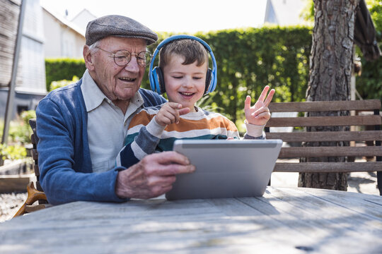 Smiling senior man with grandson using tablet PC at table