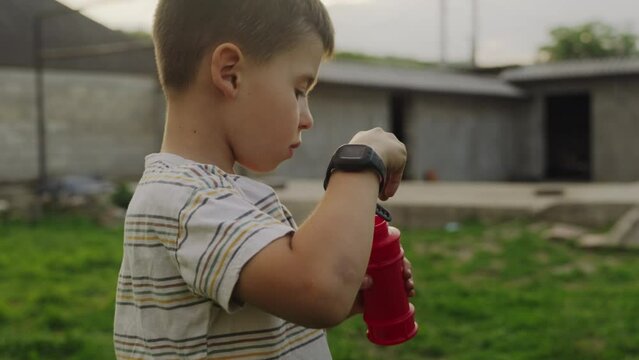Side view of a boy playing with his little sister while doing soap bubles outdoor in the garden.