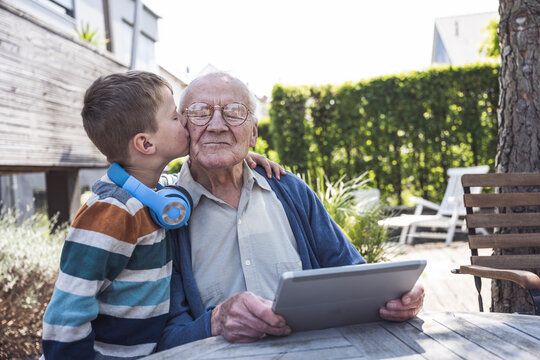 Boy kissing grandfather sitting with tablet PC at table