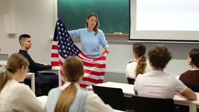 Geography lesson in school class - teacher talks about United States of America, holding a flag in his hands. High quality 4k footage