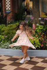 Adorable little girl in gorgeous dress spin around. Happy kid walking in open mall