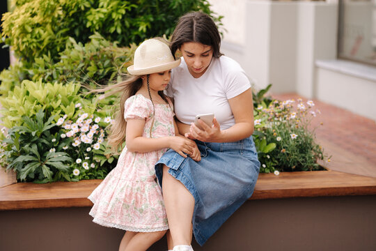 Mom and daughter looking pictures on phone. Beautiful girls using phone outdoor