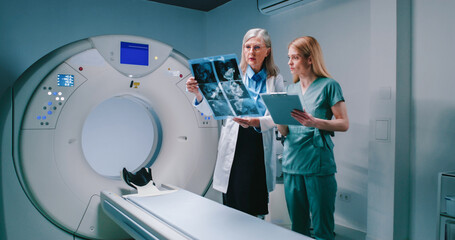 Head doctor consults with nurse. Female doctor holds results of MRI of brain. Medical workers in...