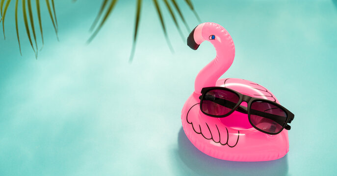 Sunglasses special offer, promo. Trendy sunglass on inflatable flamingo on blue background with palm leaves. Trendy Fashion summer accessories. Copy space. Summer sale. Optic store discount poster