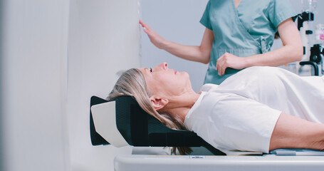 Back shoot of female patient lying down at CT scanner bed. Doctor is performing magnetic resonance...