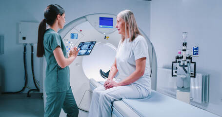 Male doctor and female patient are having talk at tomography chamber. African American doctor is...