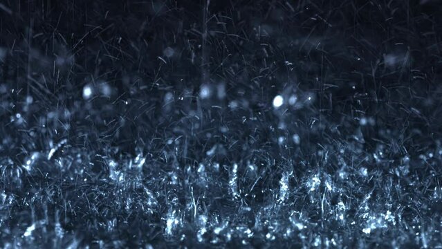 Heavy rain falling in front of the camera against black screen. Raindrops splashing. Rain closeup vfx insert. Practical seamlessly loopable footage. Heavy rainstorm hitting black surface.