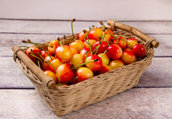 Yellow fresh cherry with leaves in a basket against a gray wooden background.