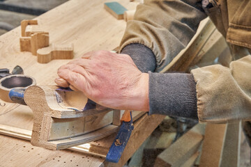 Carpenter sands bending wooden railing with sandpaper in workshop closeup. Senior master makes detail of spiral staircase for home interior
