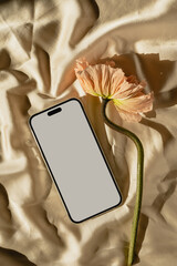 Flatlay of blank screen mobile phone and poppy flower on tan golden fabric. Flat lay, top view. Copy space mockup template