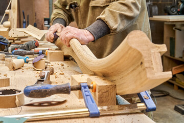 Carpenter sands bending wooden railing with sandpaper in workshop closeup. Senior master makes...