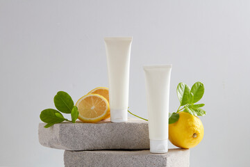 Empty label white tubes arranged with fresh leaves and lemon on stone podiums. Lemon (Citrus limon) contain high concentrations of vitamin C