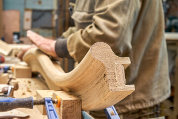 Carpenter sands bending wooden railing with sandpaper in workshop closeup. Senior master makes detail of spiral staircase for home interior - obrazy, fototapety, plakaty