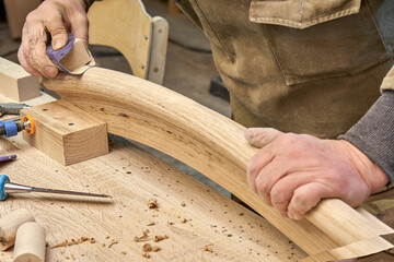 Carpenter sands bending wooden railing with sandpaper in workshop closeup. Senior master makes detail of spiral staircase for home interior - 616935786