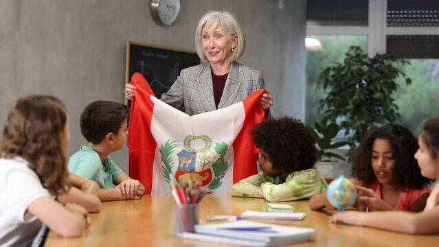 Female teacher showing peruvian flag to kids in geography class kids