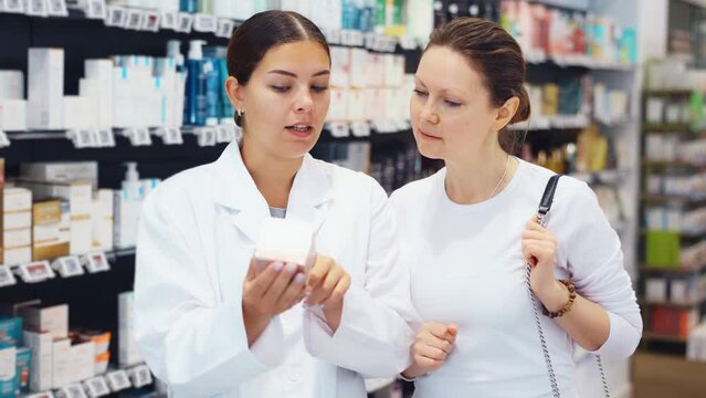 Woman listens to pharmacist s speech about products for daily facial skin care and examines packaging of cream