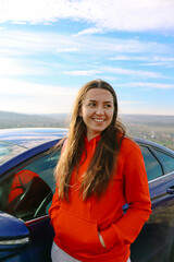 A woman stands near the car.Girl with a auto.Woman driver.Woman auto enthusiast.Driving a car as a hobby.Renting a car.The girl has long hair.The wind blows hair.
car rent.driving school.
happy girl.