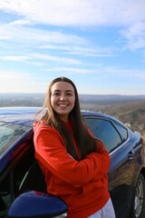 A woman stands near the car.Girl with a car.Woman driver.Woman auto enthusiast.Driving a car as a hobby.Renting a car.The auto stands in nature.The girl has long hair.Driving school.Rent a auto.travel