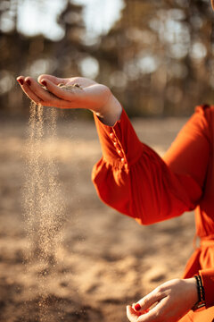 Eine junge Frau in oranger Kleid lässt den Sand durch die Finger fliesen