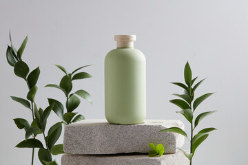Stone podiums stacked on each other with a bottle placed on. Decorated with many dark green leaves. Blank label for product mockup