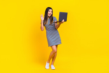 Full length photo of cute friendly woman dressed striped outfit waving arm communicating modern device isolated yellow color background