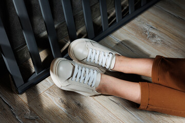 Slender female legs in pants close-up in beige casual sneakers. Women's leather shoes.