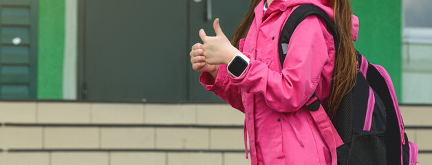 Primary school student. Little girl with a backpack near the building outdoors. Beginning of lessons. First day of autumn.