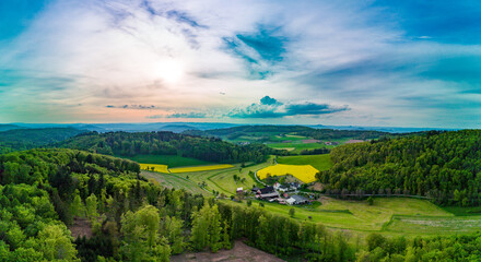 Panorama of yellow-green fields and farms in the forest in a hilly valley