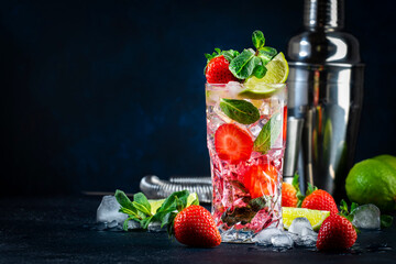 Summer strawberry mojito cocktail with lime, white rum, soda, cane sugar, mint, and ice in glass on...