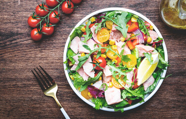 Fresh tuna and vegetable salad with cherry tomatoes, onion, sweet corn, paprika, lettuce, radicchio and arugula. Rustic wood table background, top view