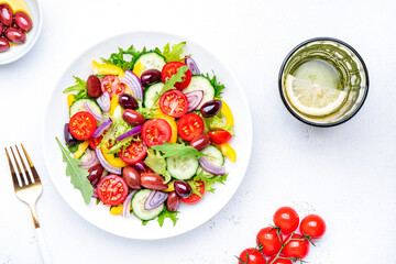 Vegan salad with kalamata olives, cherry tomato, yellow paprika, cucumber and red onion, tasty and healthy mediterranean food, low calories eating. White table background, top view